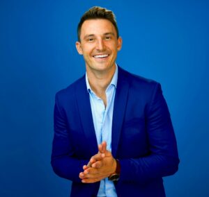 man wearing dark blue sport coat and light blue button up shirt, smiling and rubbing hands together