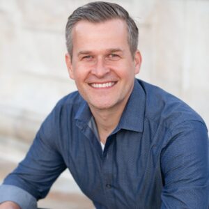 man smiling, wearing dark blue long sleeve button up shirt