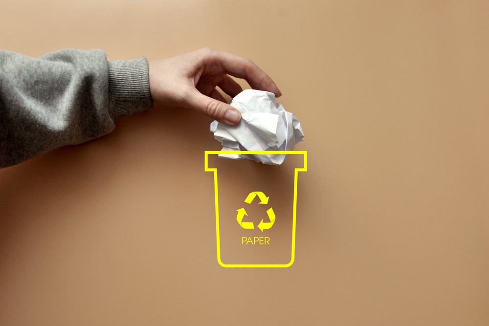 A man throws a crumpled piece of paper into a dumpster