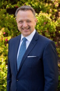 man smiling, wearing blue tie, white dress shirt and blue sport coat