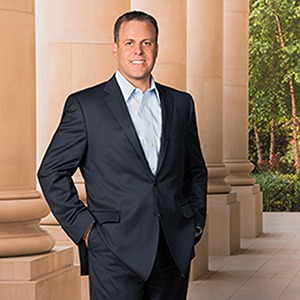 A man in a suit stands smiling at a camera