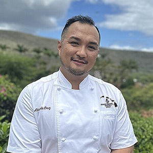 A man in a chef uniform smiles into the camera