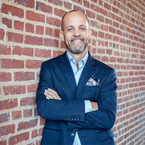 A man in a blue suit smiles into the camera