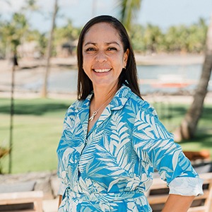 A woman in a blue shirt stands smiling into the camera