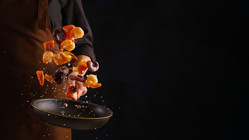 A professional chef prepares assorted seafood - octopus, shrimp and pieces of red fish