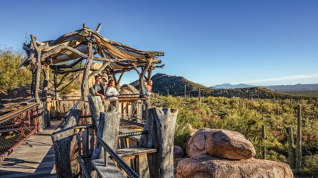 people standing on outdoor terrace, mountains in background