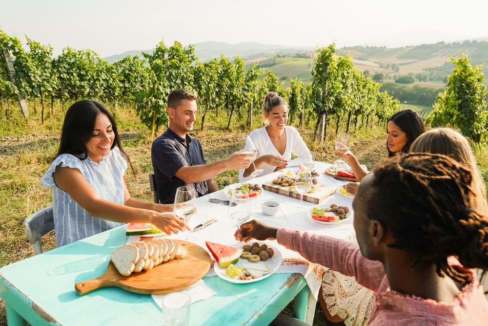 friends having fun drinking white wine and eating together with vineyard in background
