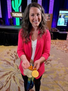 woman with pink coat showing three medals