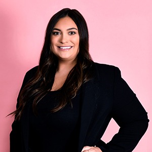 woman standing in front of pink background wearing black coat and shirt