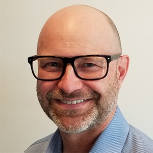 man in glasses smiling, wearing blue dress shirt