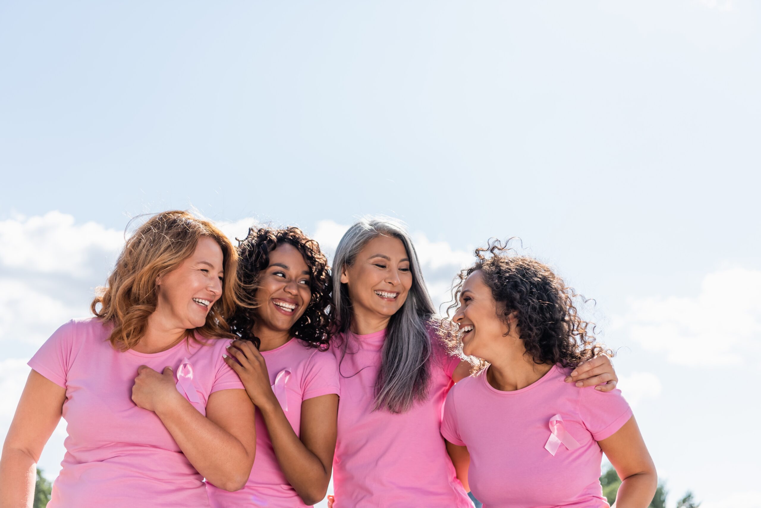 Breast cancer awareness month featured image shows four smiling women wearing pink shirts and pink ribbons
