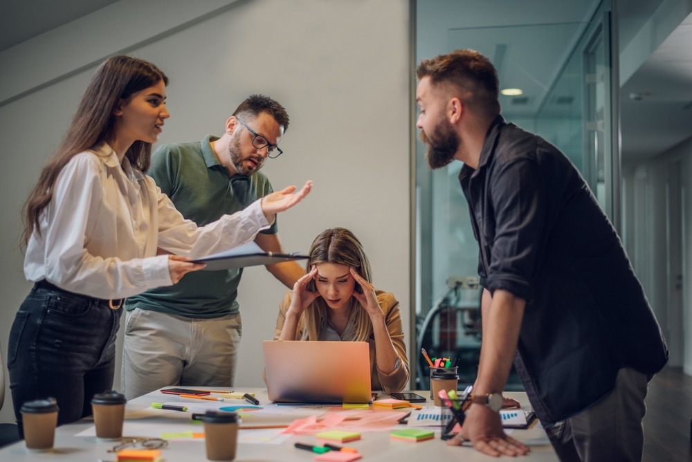 Stressed office employee next to three arguing coworkers