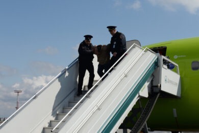 man being taken off plane by guards
