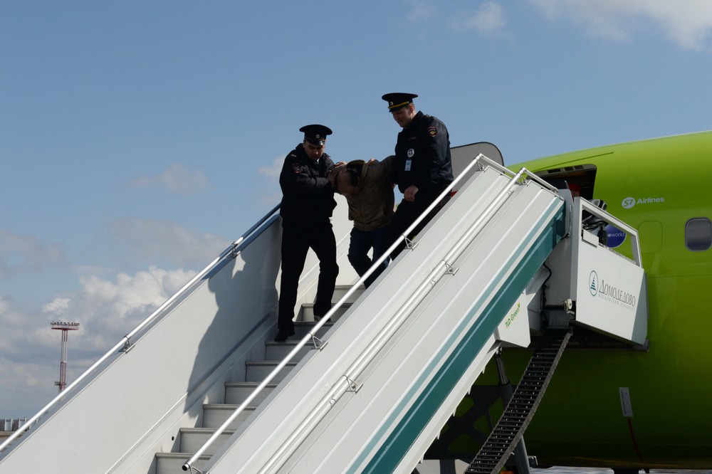 man being taken off plane by guards
