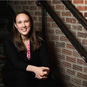 woman sitting down wearing pink top and black coat