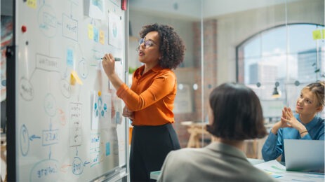 woman in orange shirt drawing on board in conference room