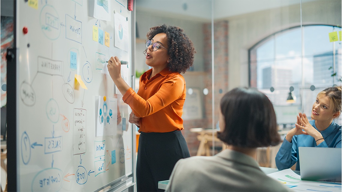 woman in orange shirt drawing on board in conference room