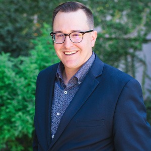 man wearing glasses and blue suit smiling