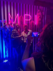 two people standing in front of purple neon letters that spell 'MPI'