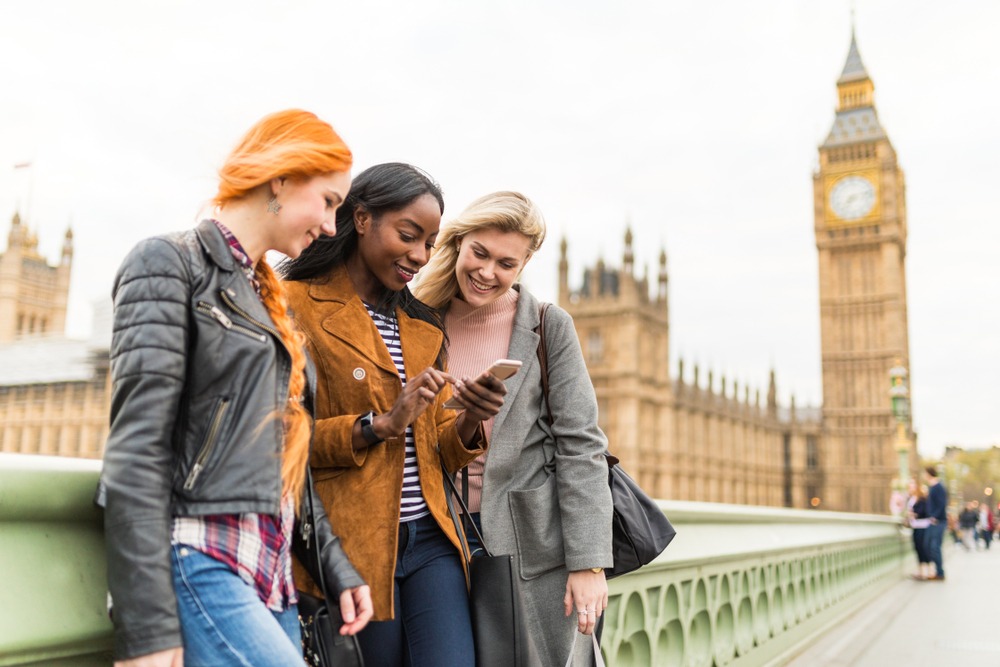 Group of girls in London looking at mobile phone with Big Ben on background