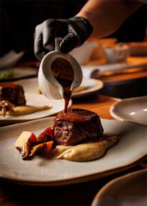 Person pouring sauce on steak