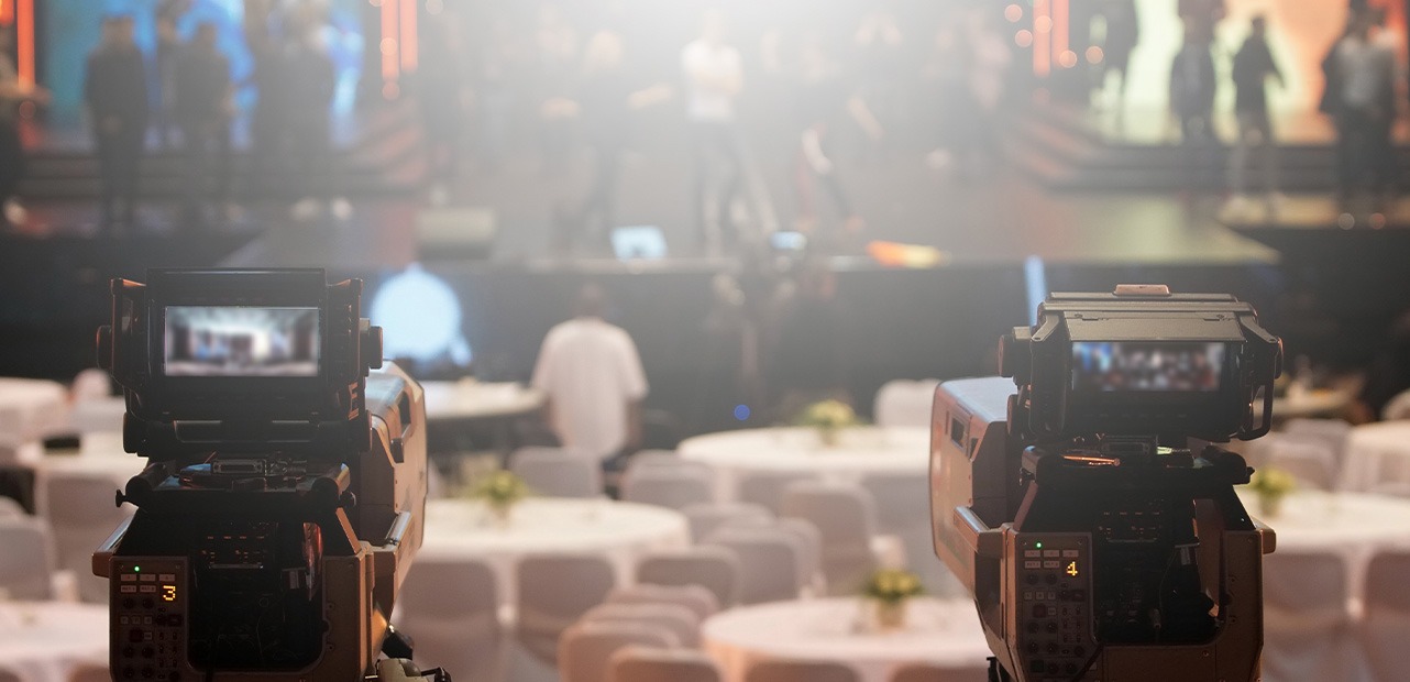 Two cameras in foreground and people working on stage in background