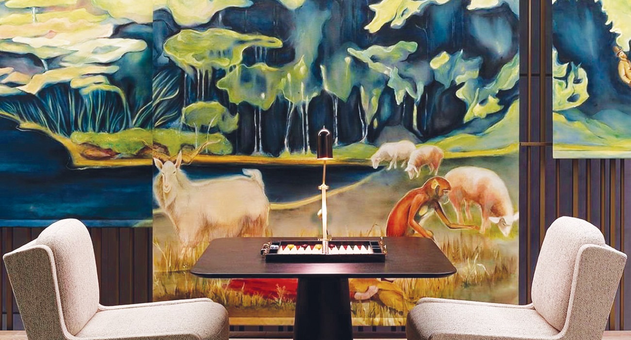 A painting of a forest on a wall in front of two chairs