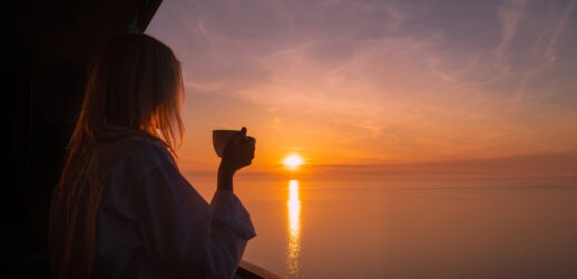 Woman holding cup of coffee and sunset