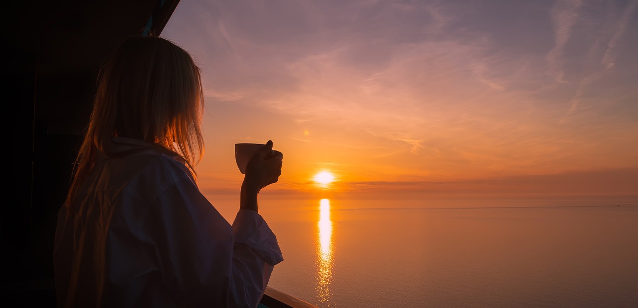 Woman holding cup of coffee and sunset